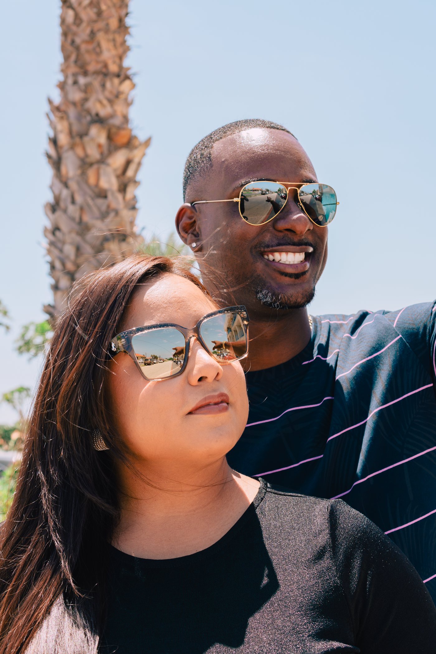 Smiling couple wearing designer sunglasses under a palm tree